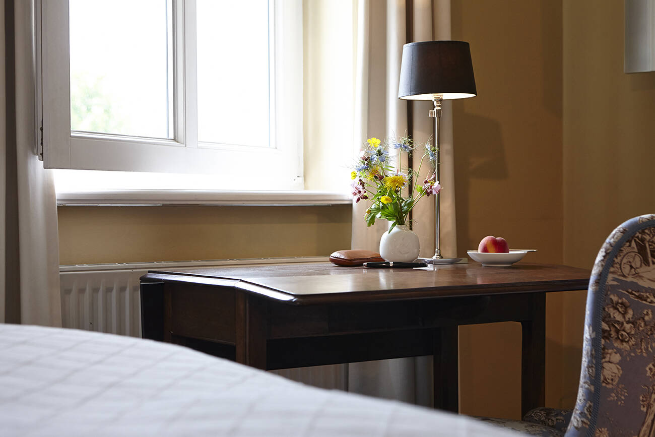 Ein Holztisch mit Vase voller bunter Blumen, einer schwarzen Stehlampe und einem Fenster im Hintergrund.