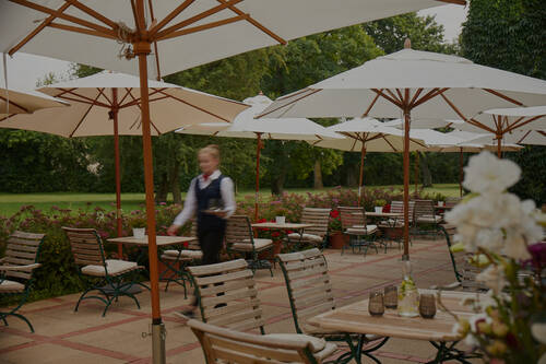 Eine großzügige Terrasse mit Holztischen, Stühlen und weißen Sonnenschirmen im gepflegten Garten.
