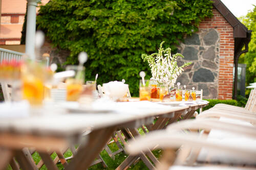 Ein langer Holztisch im Garten ist mit Getränken und Blumen dekoriert, ideal für sommerliche Feste.