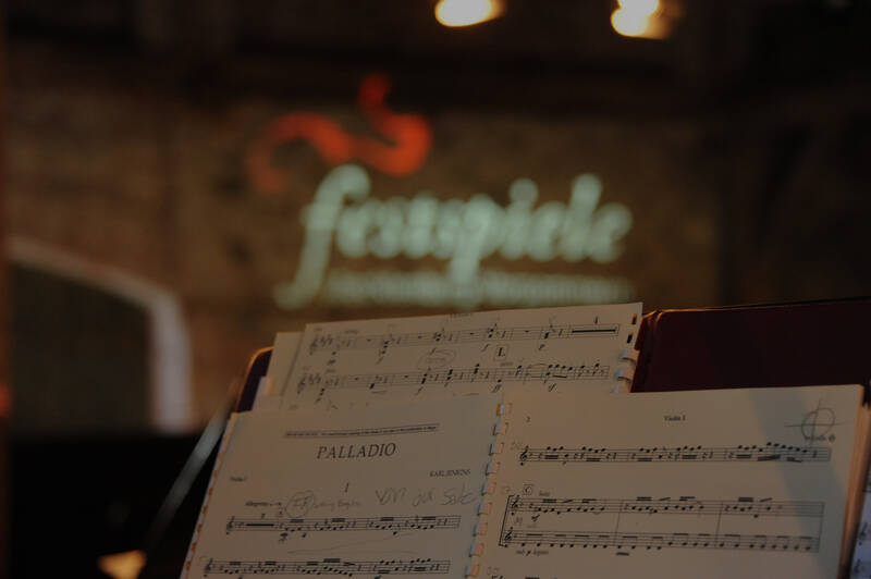 Ein Notenblatt mit dem Titel "Palladio" auf einem Notenständer, im unscharfen Hintergrund ist der Schriftzug "Festspiele".