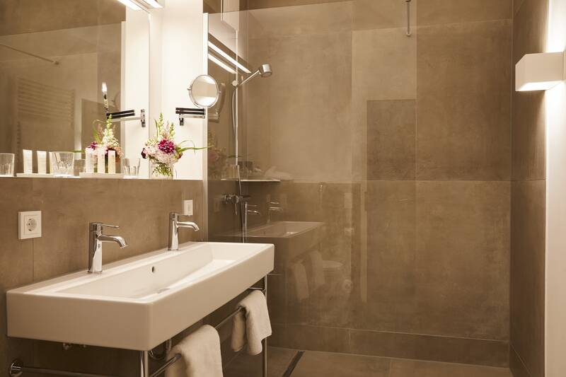 Ein großes Bad mit einer begehbaren Dusche, einem Doppelwaschbecken und frischen Blumen auf dem Spiegelrand.
