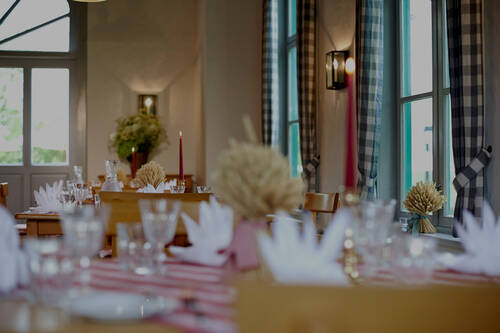 Elegant gedeckte Tische mit Kerzen und weißen Servietten im hellen Restaurant mit karierten Vorhängen.