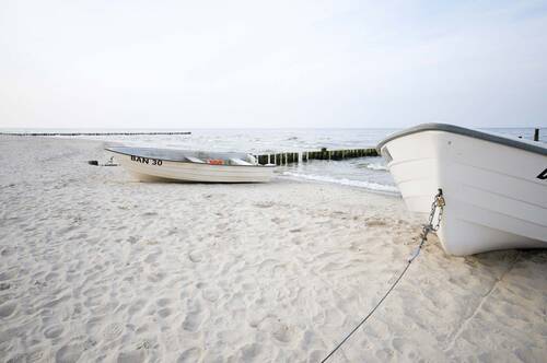 Zwei weiße Boote liegen auf hellem Sandstrand am Meer, die See ist ruhig und klar.