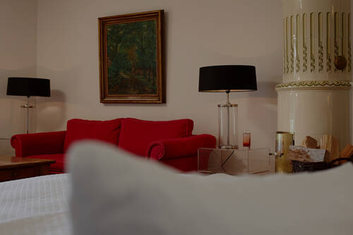 Ein eleganter Raum mit einem roten Sofa, schwarzen Lampen und weißem Kaminofen – geschmackvoll und gemütlich eingerichtet.
