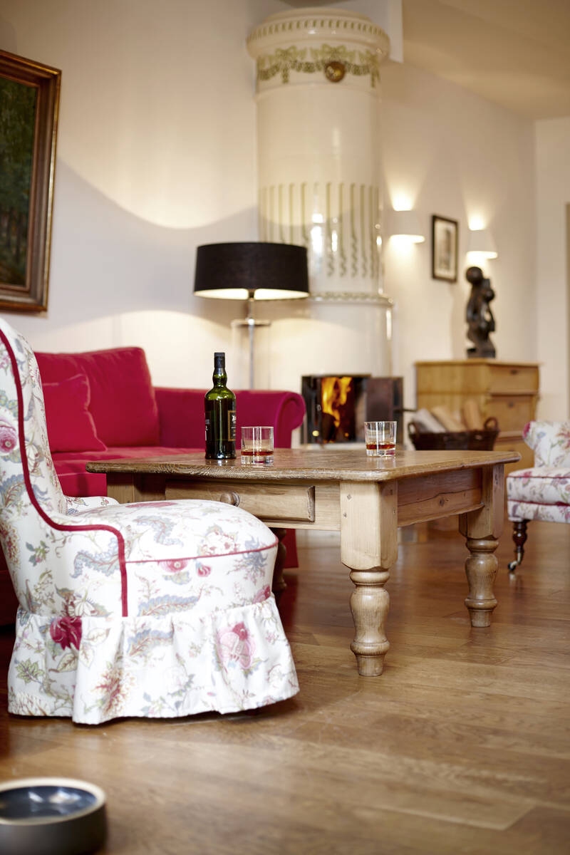 Ein helles Gutsherrenzimmer im Gutshaus Stolpe mit roten Sofas, gemusterten Sesseln und einem weißen Kamin.