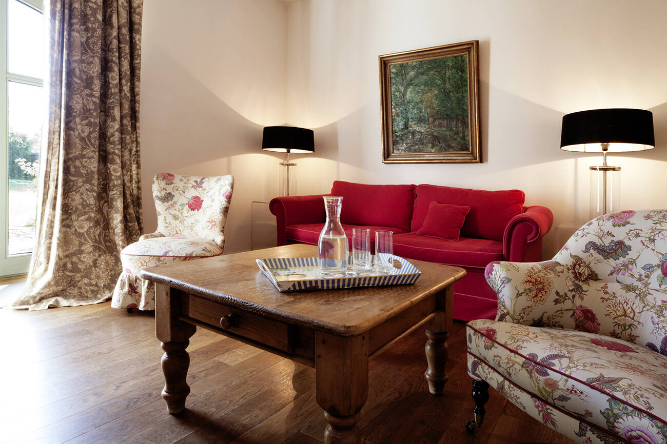 Ein gemütliches Wohnzimmer mit rotem Sofa, gemusterten Sesseln und Holztisch in harmonischen Farben.