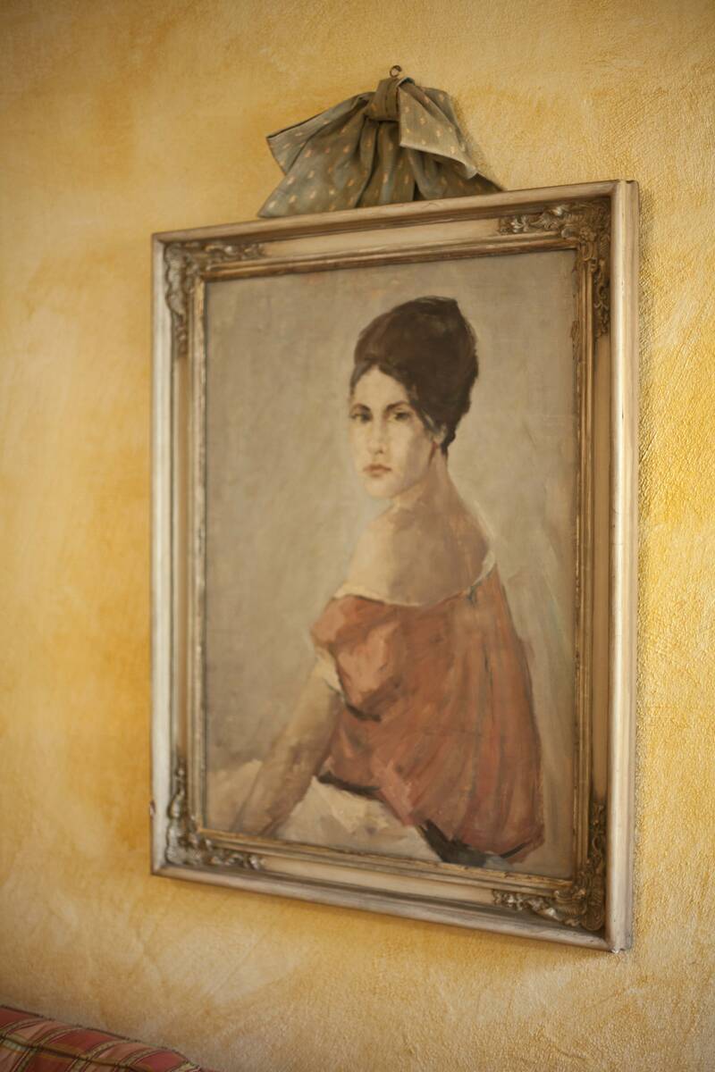 Ein klassisches Gemälde einer Frau mit hochgestecktem Haar und rotem Kleid in vergoldetem Rahmen an einer gelben Wand.
