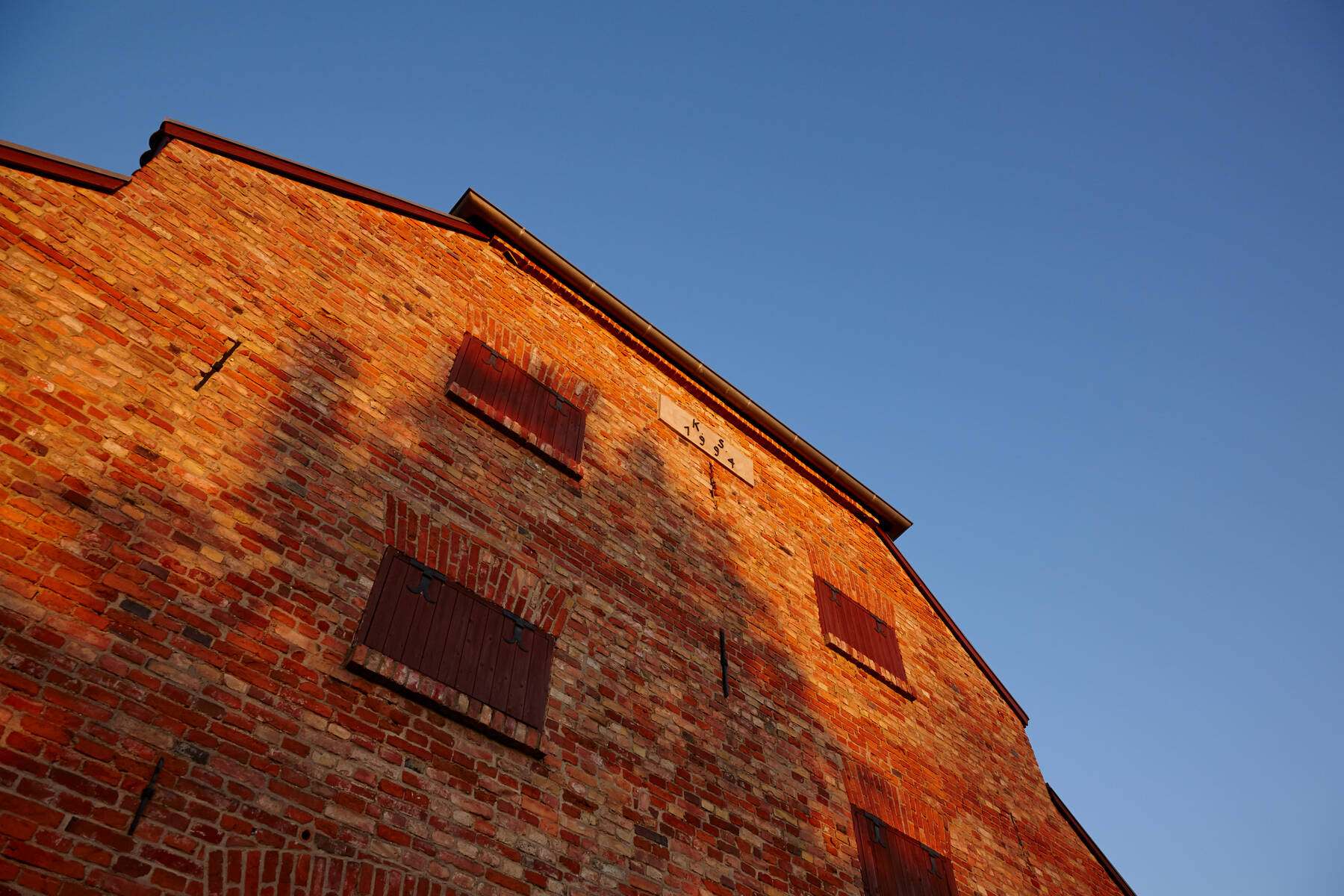 Eine historische Backsteinfassade mit kleinen Fenstern, im goldenen Licht der Abendsonne – ländliche Architektur mit Geschichte.