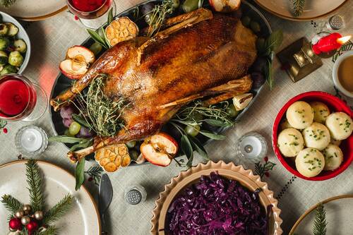 Eine gebratene Gans auf einer Festtafel mit Klößen, Rotkohl, Äpfeln und Kräutern – ein traditionelles Weihnachtsgericht.