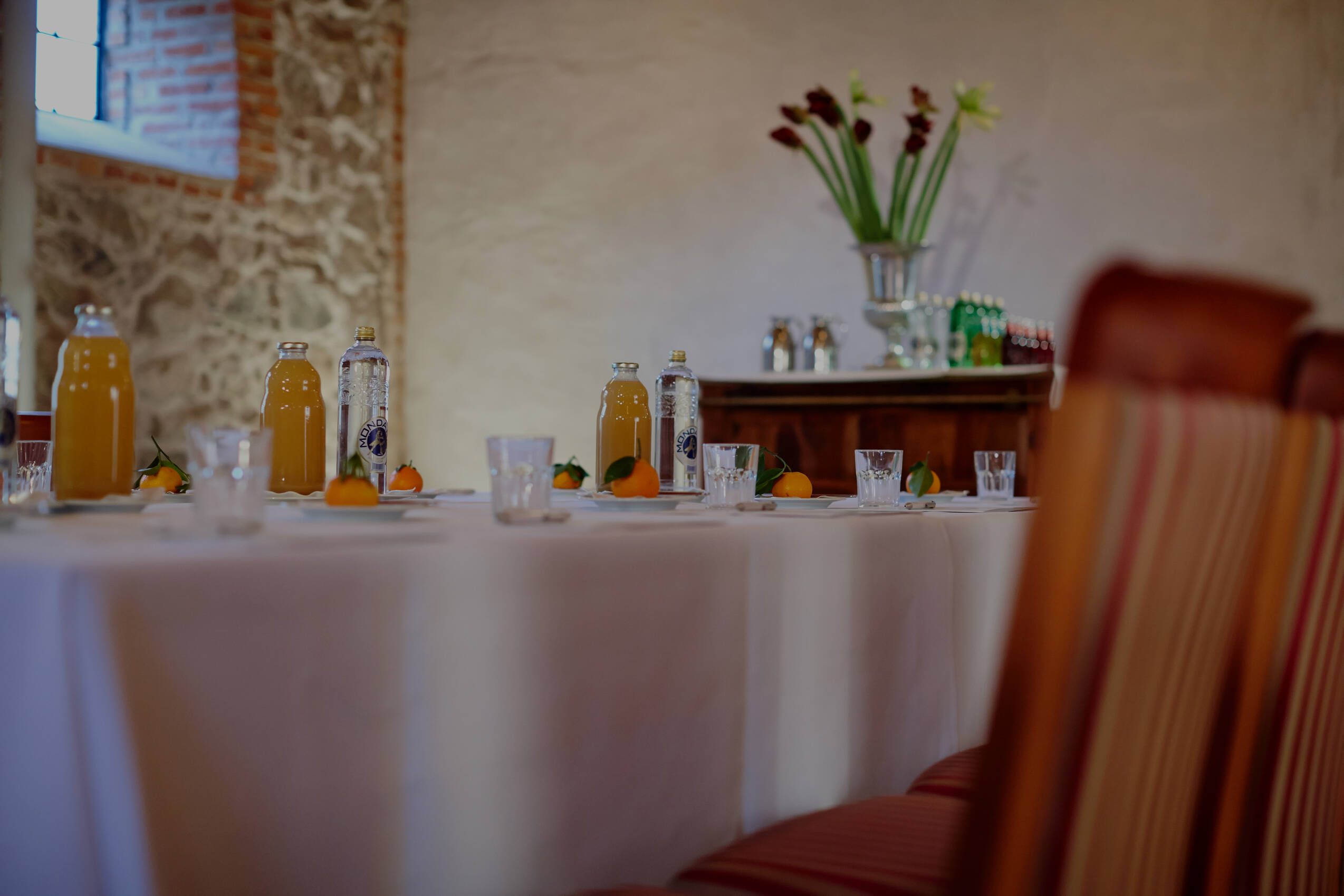 Ein gedeckter Tisch mit Orangensaft, Wasserflaschen und kleinen Früchten in einem stilvollen Tagungsraum.