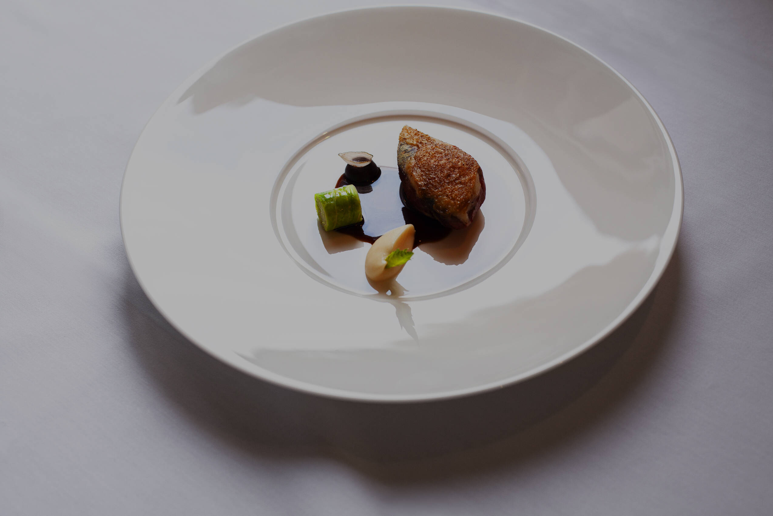 Ein feines Gericht mit Fleischstück, Gemüse und Sauce kunstvoll angerichtet auf weißem Teller in Gourmetrestaurant Stolpe.