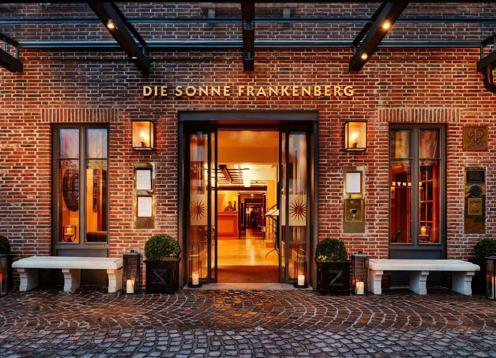 Ein beleuchteter Eingangsbereich des Hotels Die Sonne Frankenberg mit Backsteinfassade und warmem Licht.