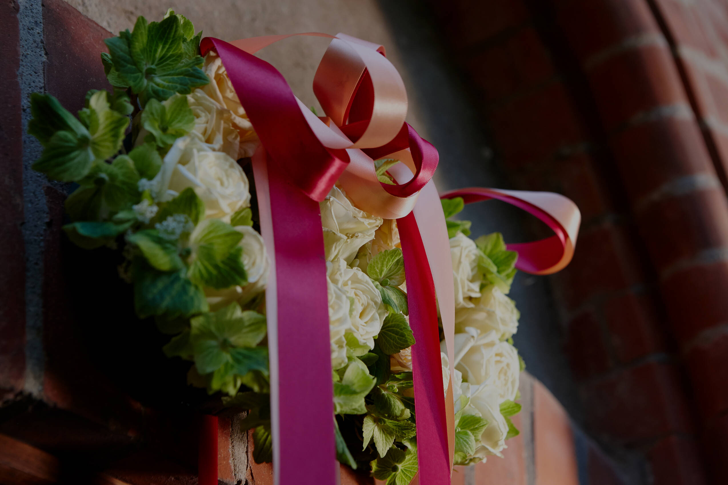 Eine Detailaufnahme einer festlichen Blumendekoration mit weißen Rosen, grünen Blättern und rosa Bändern in einer romantischen Hochzeitslocation in Mecklenburg-Vorpommern.