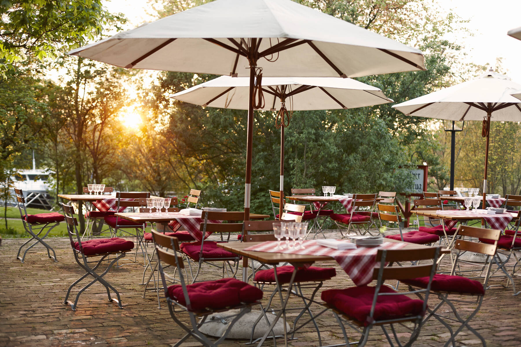 Eine romantische Terrasse mit Holzstühlen, roten Sitzkissen und großen Sonnenschirmen im warmen Licht des Sonnenuntergangs.