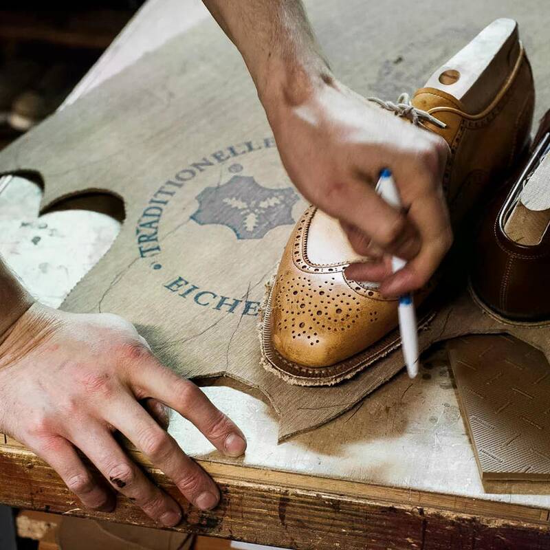 Ein Handwerker markiert sorgfältig Leder für einen maßgefertigten Schuh auf einem Werkstatttisch.
