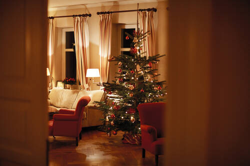 Ein Wohnzimmer mit einem leuchtenden Weihnachtsbaum, roten Sesseln, einem Sofa und warmem Licht im Gutshaus Stolpe.