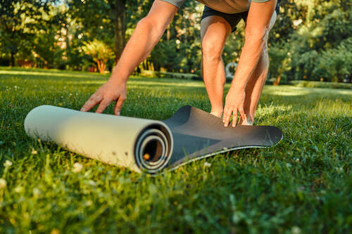 Eine Person bereitet auf einer Wiese eine Yogamatte vor – Achtsamkeit, Bewegung und Naturverbundenheit.