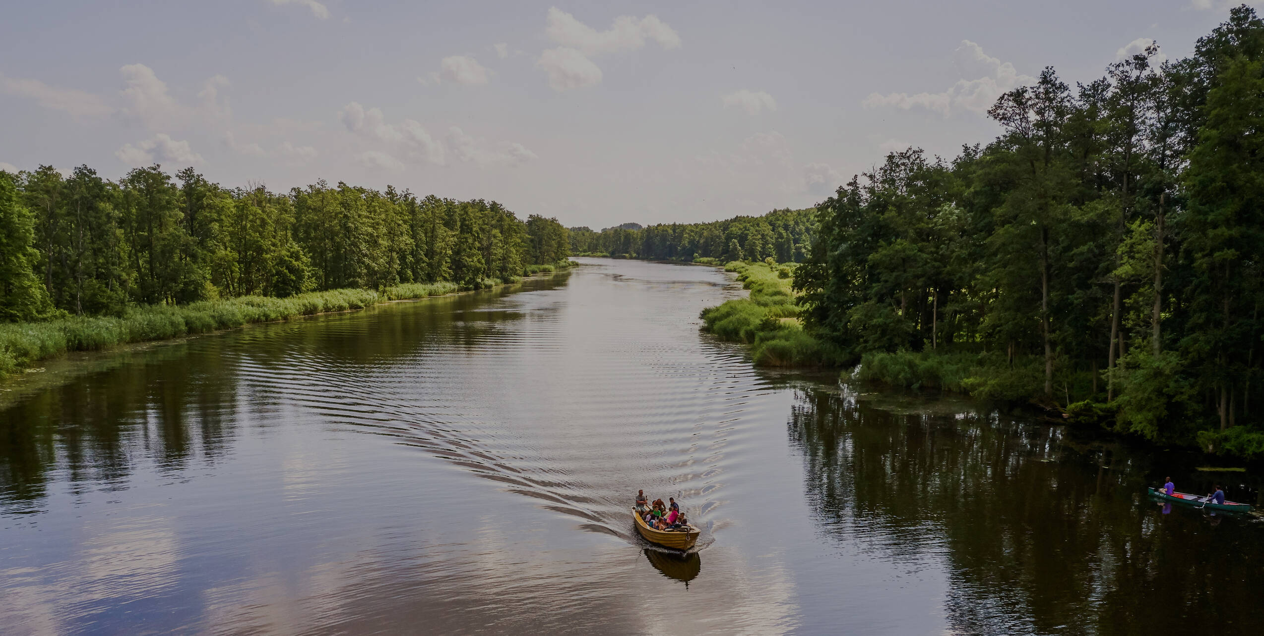 Ein kleines Boot mit Gästen gleitet über einen breiten Fluss, umgeben von dichter Natur – Entspannung und Entdeckung pur.
