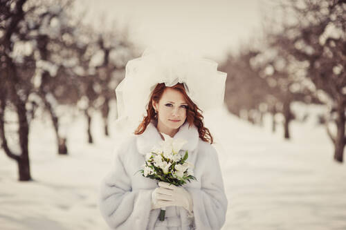 Eine Braut im Schnee mit Blumenstrauß in romantischer Hochzeitslocation Mecklenburg-Vorpommern.