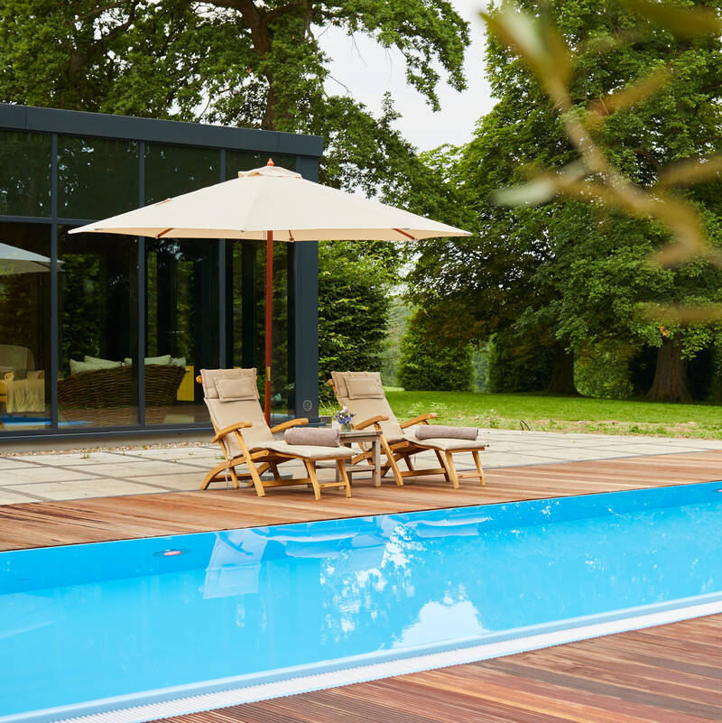 Zwei bequeme Liegestühle am blauen Pool, umgeben von Natur – perfekte Entspannung in einem romantischen Hotel Norddeutschland.