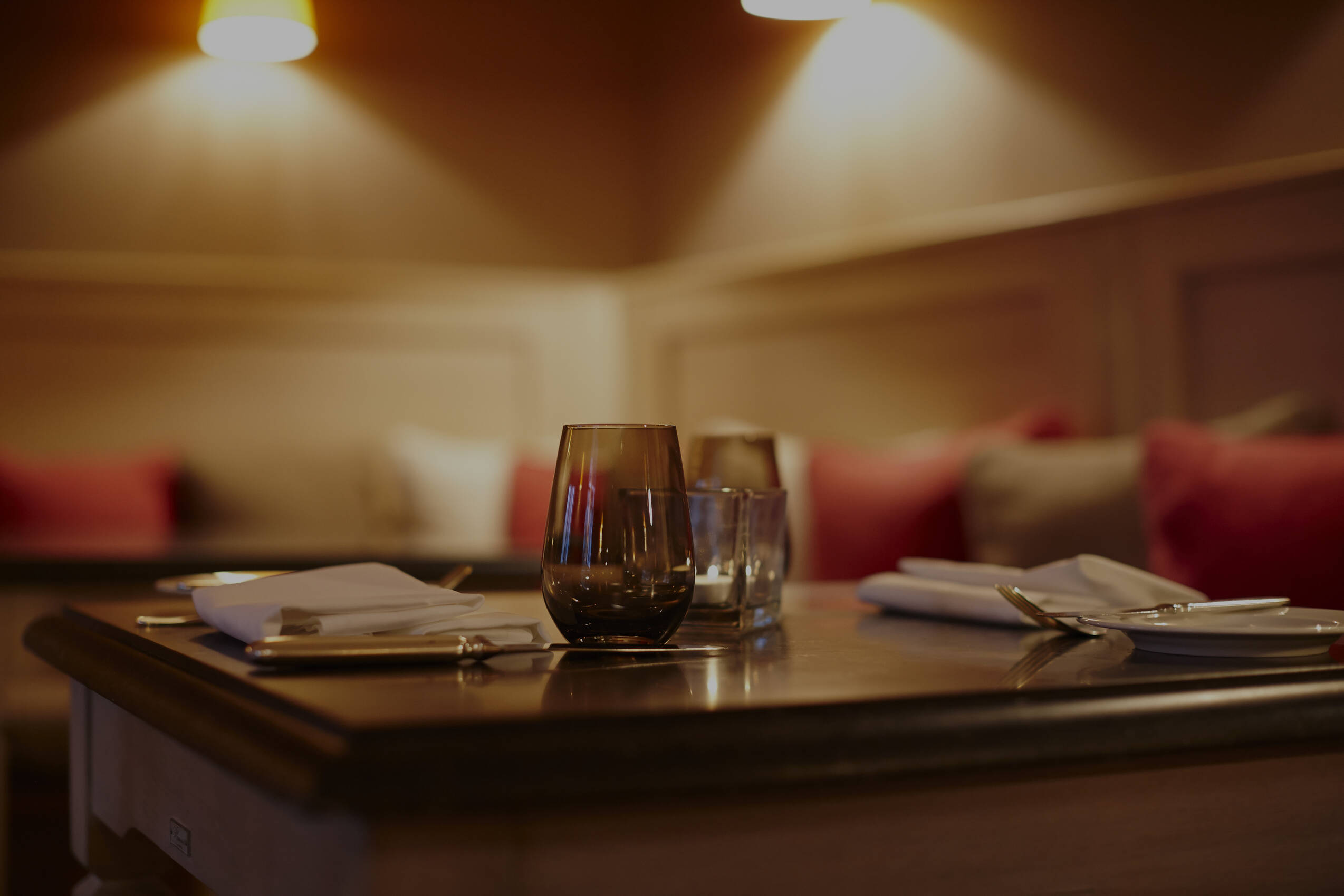 Ein elegant gedeckter Tisch mit Gläsern und Stoffservietten in gedämpftem Licht einer gemütlichen Lounge.
