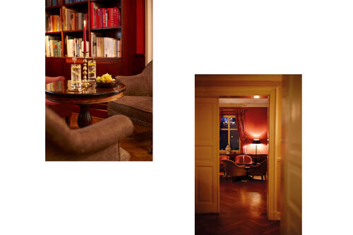 Ein stimmungsvolle Hotelbar mit rotem Licht, gemütlichen Sesseln, einem Bücherregal und Gläsern auf einem Tisch.