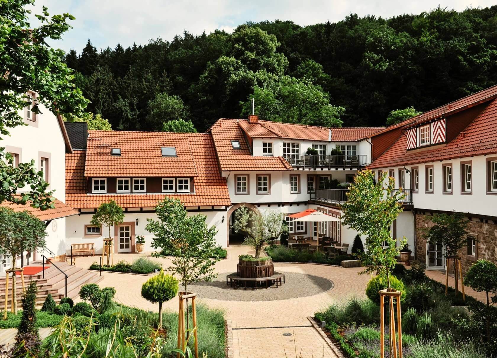 Ein gepflegter Innenhof mit roten Dächern, Bäumen und Sitzbereichen – harmonische Kombination aus Natur und Architektur.