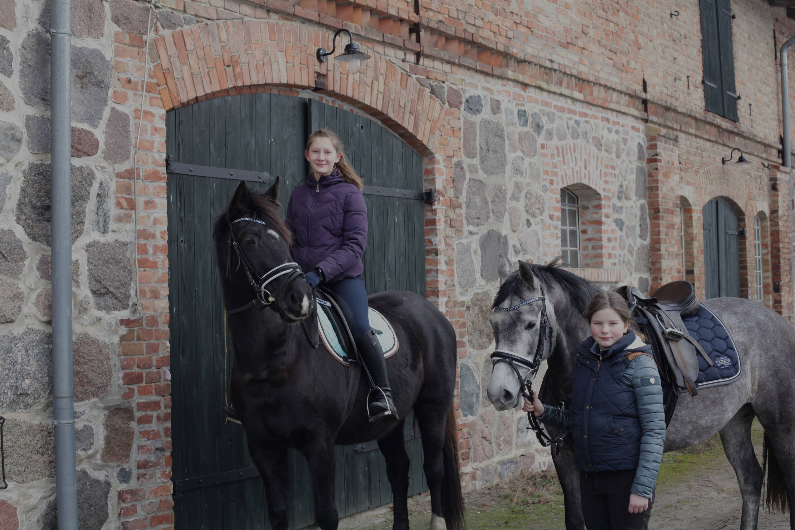 Zwei Mädchen mit Pferden vor dem Gutshaus Stolpe – authentisches Reiten im Urlaub in idyllischer Landhausatmosphäre.