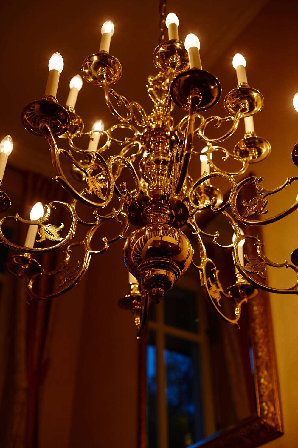 Ein prächtiger, goldener Kronleuchter mit brennenden Kerzen sorgt für warmes Licht und elegante Atmosphäre.