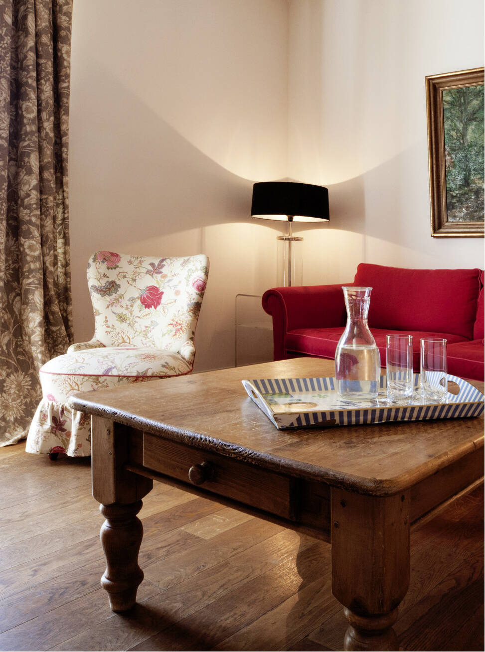 Ein stilvoller Raum mit einem roten Sofa, floralen Sessel und Holztisch – warme Beleuchtung und gemütliches Flair.
