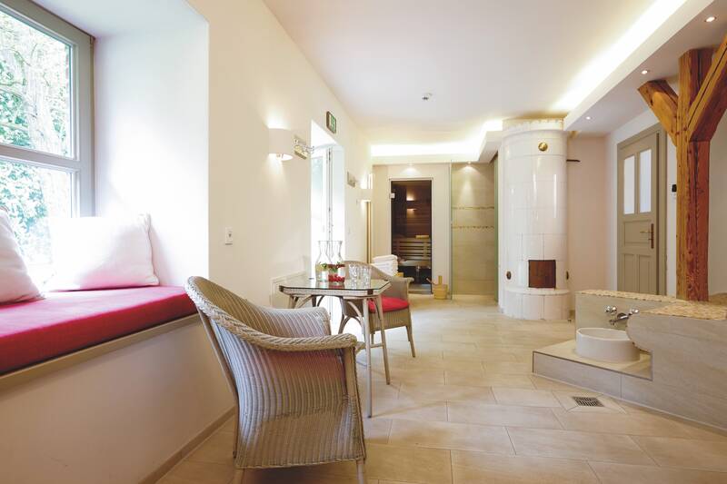 Ein heller Wellnessbereich mit Rattan Stühlen, Fensterbank mit Kissen und Zugang zur Sauna.