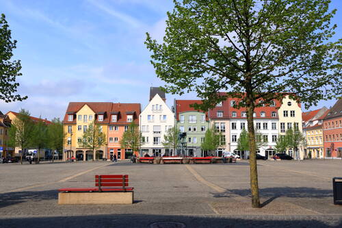 Ein Platz in Anklam mit Bäumen, bunten Fassaden und Bänken in einer ruhigen Altstadt bei mildem Morgenlicht.