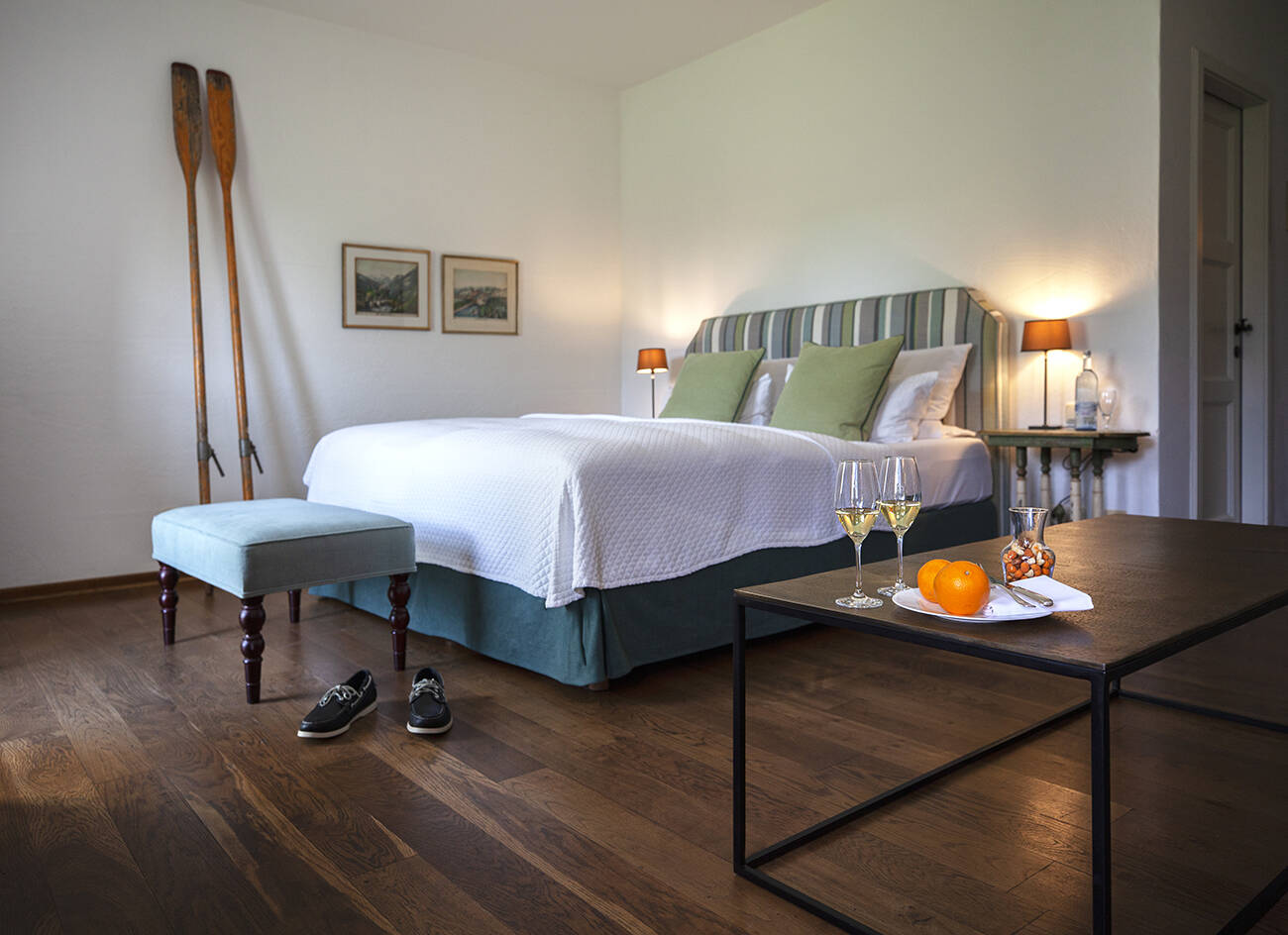 Ein helles Gartenzimmer mit einem Doppelbett, Holzfußboden, Tisch mit Obst und Getränken, dekoriert mit Rudern.