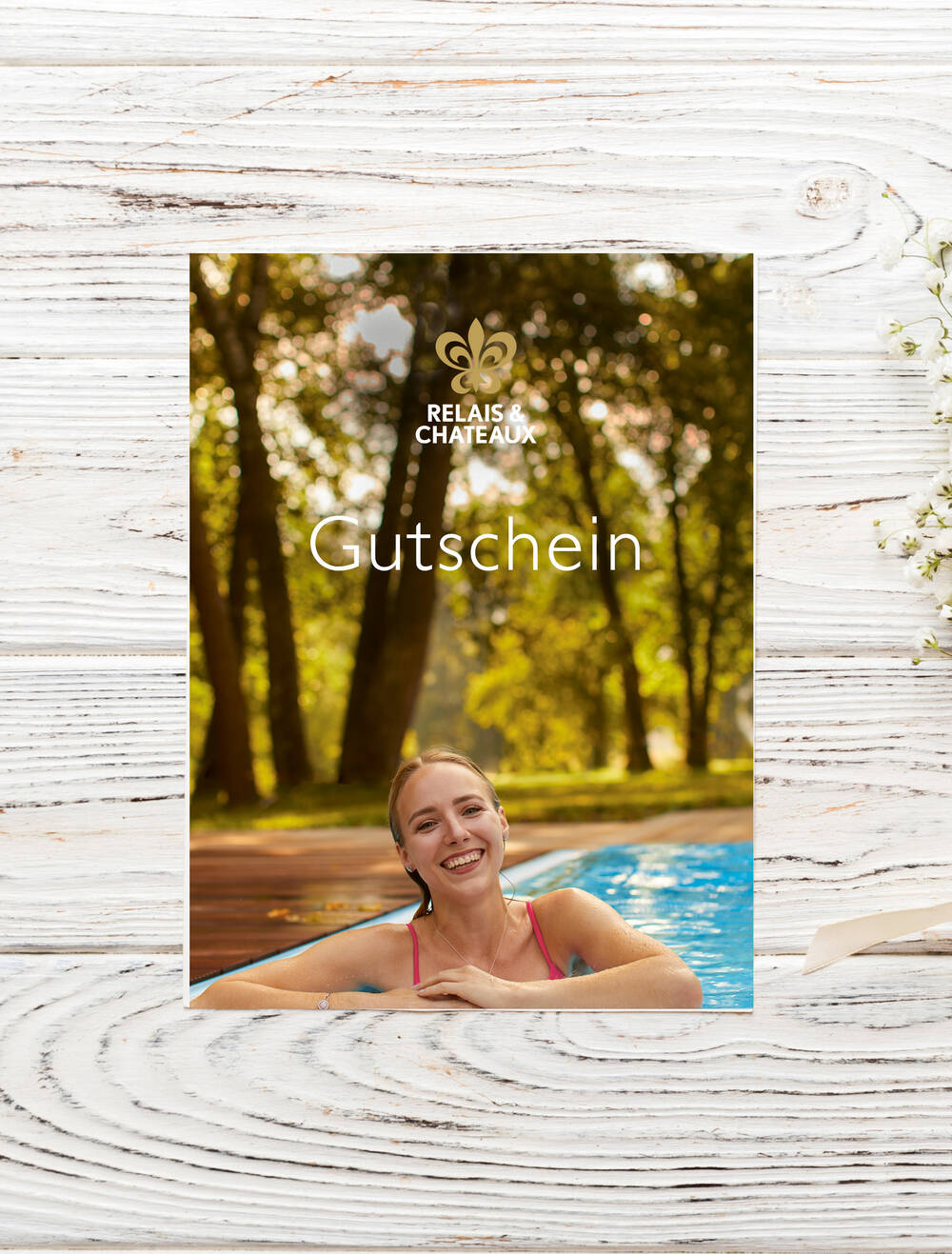 Gutschein von Relais & Châteaux mit lachender Frau im Pool, umgeben von grünem Park und Sonnenlicht im Hintergrund.