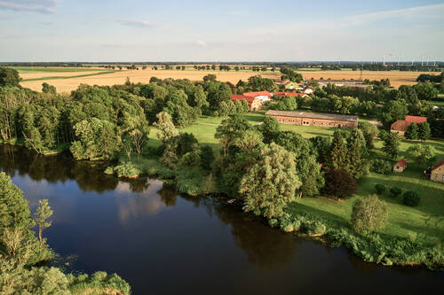 Eine idyllische Luftaufnahme des Gutshaus Stolpe – ein Hotel mit Pferden, gelegen inmitten weiter Felder und am ruhigen Peenetal.